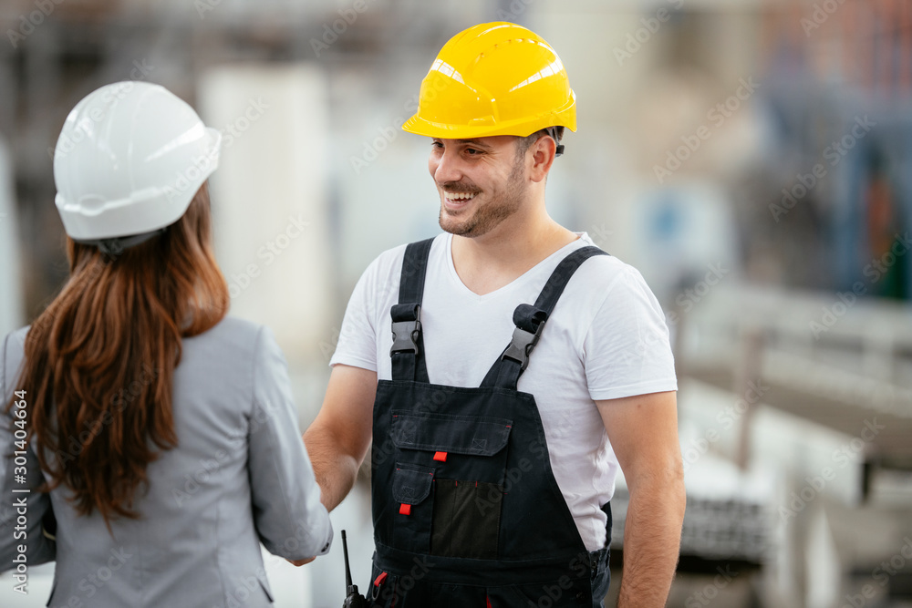 Architect and worker working on project. Colleagues handshaking in factory. Architect and worker working on project. Colleagues handshaking in factory.