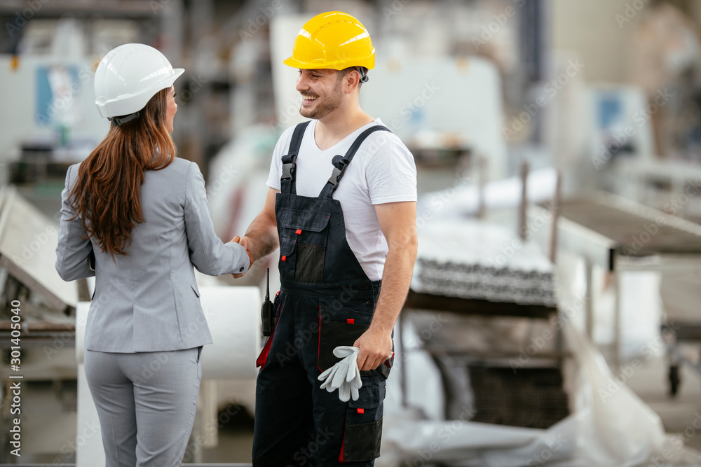 Architect and worker working on project. Colleagues handshaking in factory. Architect and worker working on project. Colleagues handshaking in factory.