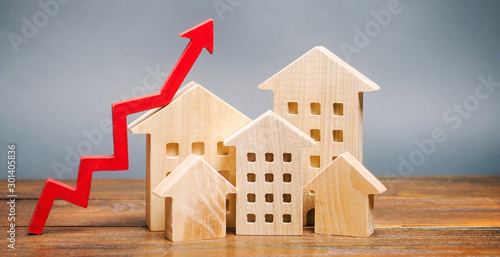 Miniature wooden houses and red arrow up. The concept of increasing the cost of housing. High demand for real estate. The growth of rent and mortgage rates. Sale of apartments. Population grows