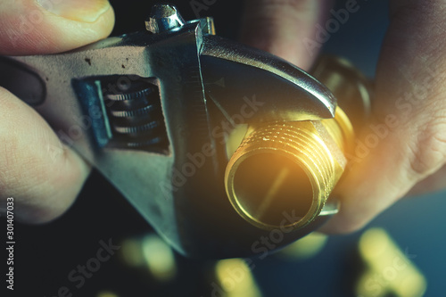 Plumber hands screwing nut of pipe over plumbing tools background. Concept of repair and technical assistance. Close up shot. Brutal atristic toning