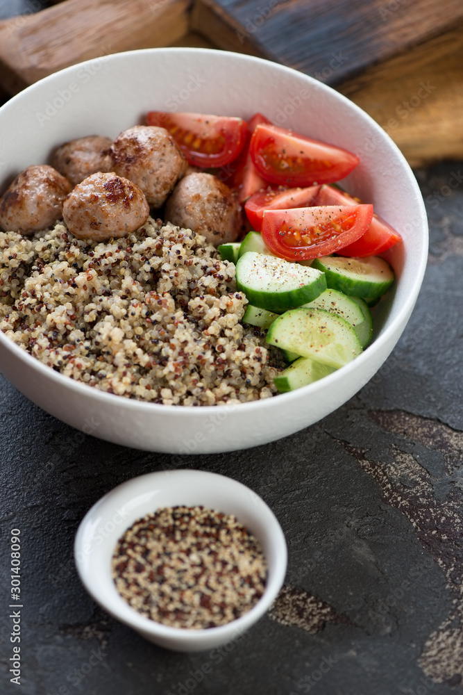 White bowl with fried meatballs, quinoa and vegetables, vertical shot on a brown stone surface, close-up White bowl with fried meatballs, quinoa and vegetables, vertical shot on a brown stone surface, close-up