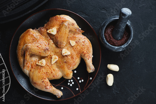 Black plate with pan fried chicken tapaka, flatlay over black stone background, horizontal shot photo