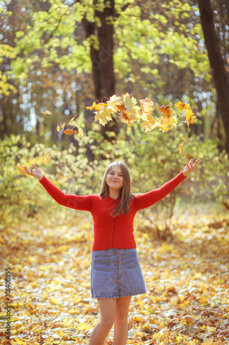Girl throws autumn leaves in forest and smiles.