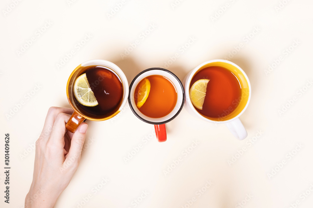 Cups with tea with lemon on a beige background. Hot winter drinks concept. One of the cups is held by a hand. Top view, minimalism, flat lay. Place for text.
