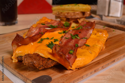 CLASSIC BREADED FRIED MEAT , KNOWN IN ARGENTINA AS MILANESA, BACON AND CHEDDAR CHEESE, SERVED WITH FRENCH FRIES ON A WOODEN TABLE