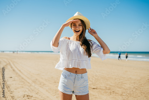 the girl in the hat with her hair looks joyfully at someone on the beach. Recognition emotion