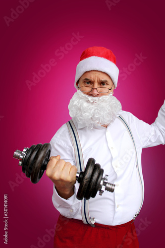 Santa Claus in glasses, in a white shirt, shakes muscles with dumbbells, Christmas and sports concept, close-up