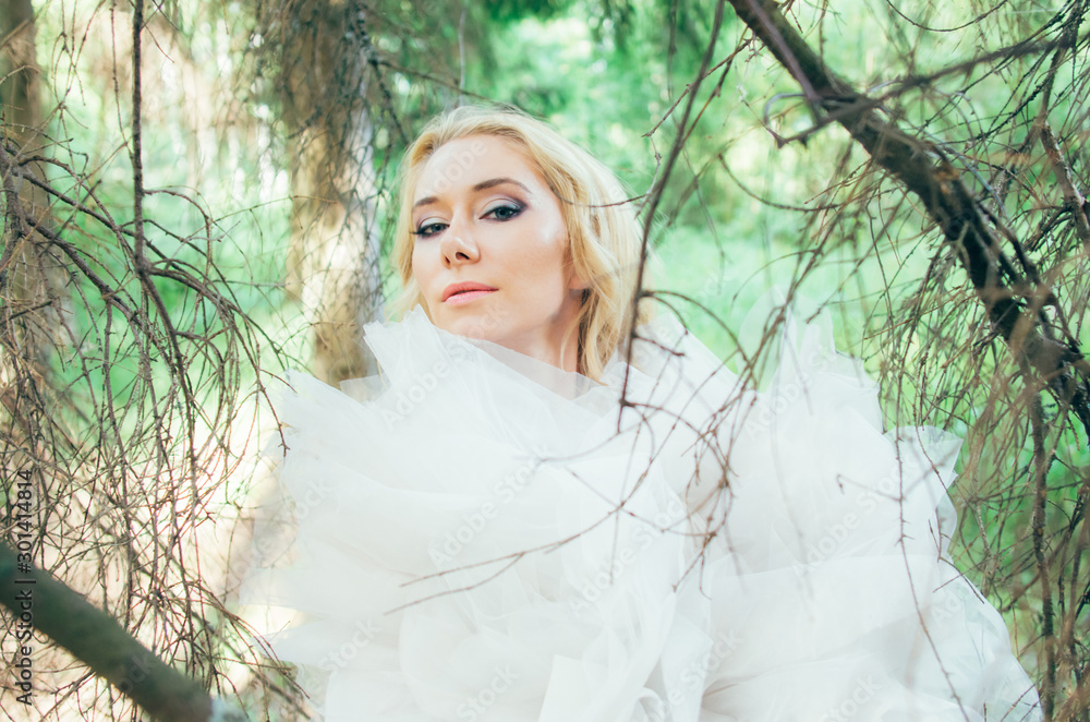 Naklejka premium Portrait of young blond bride in forest through branches