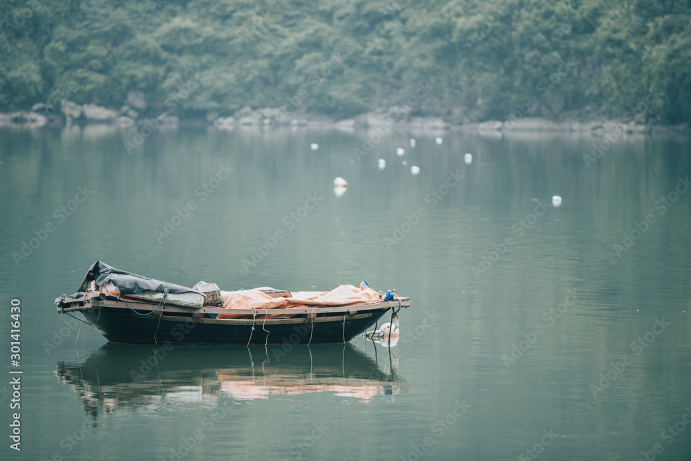 A small little wooden rowing boat left afloat in the emerald green waters near Cat Ba Village in Ha Long Bay, North Vietname