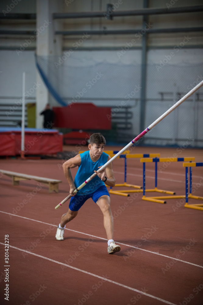 Pole vaulting indoors - young man running on the runway holding a pole