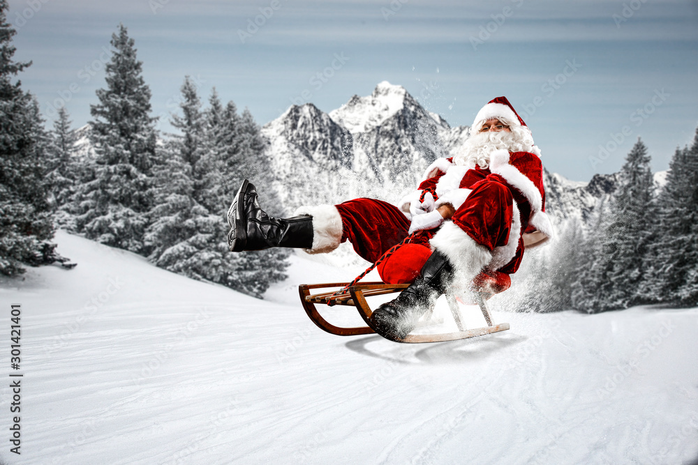 Red Santa Claus riding a wooden sled. An older man with a beard delivers presents to a child. Winter mountains landscape and snow-covered trees with frost. Fir branches, winter time. Christmas spells - obrazy, fototapety, plakaty 