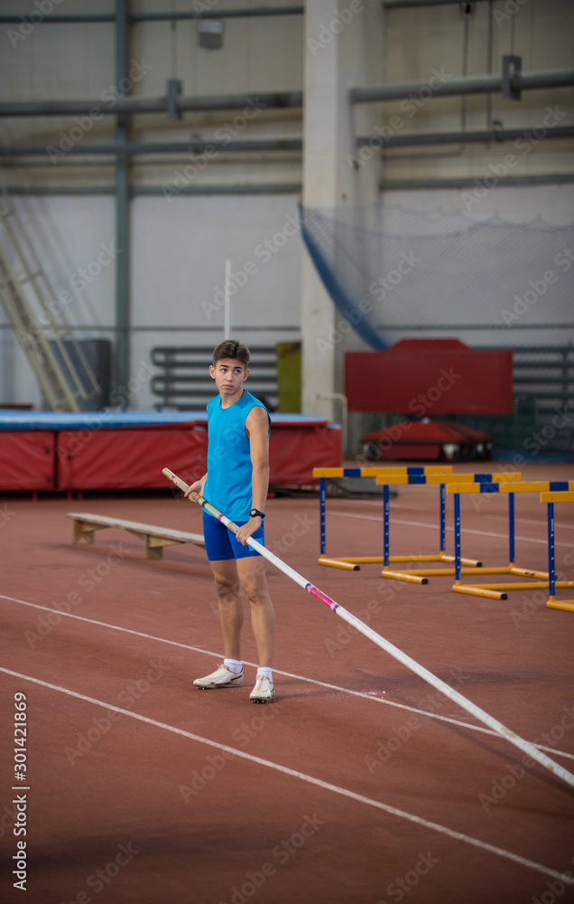 Pole vaulting indoors - young man in blue shirt standing on the runway holding a pole