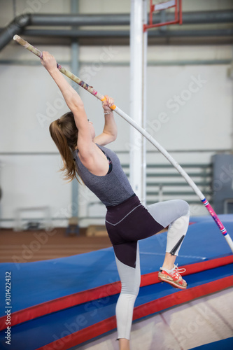 Pole vaulting indoors - young sportive woman with ponytail leaning on the pole and about to jump