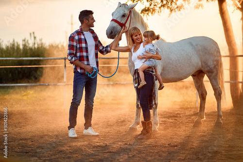 Smiling family with girl in a horse farm petting horses photo