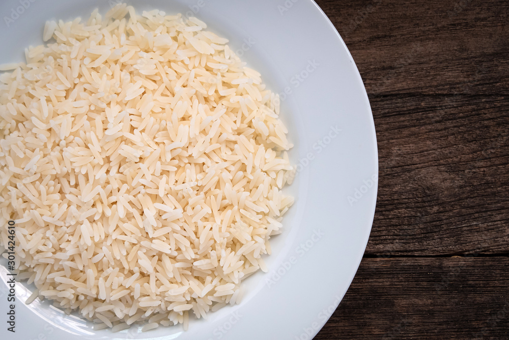 Parboiled cooked rice in a white ceramic plate. Parboiled rice on a wooden table. Parboiled rice Products exported from Thailand. Parboiled rice ligth colour. Parboiled rice close up shot. top view. Parboiled cooked rice in a white ceramic plate. Parboiled rice on a wooden table. Parboiled rice Products exported from Thailand. Parboiled rice ligth colour. Parboiled rice close up shot. top view.