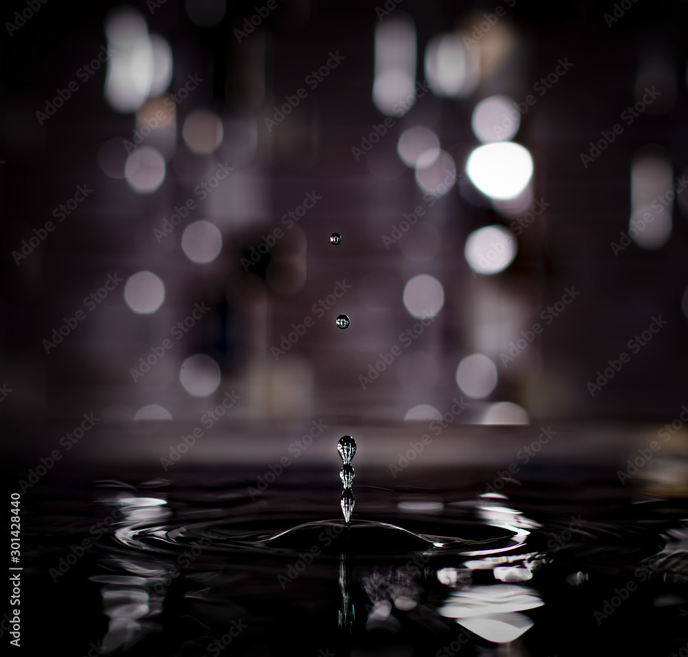 Beautiful dark mysterious image of stop motion three merging water drops chased by two others drops in dark bokeh abstract colored backround.
