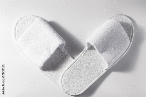 Top view of white slippers on a white wooden background. Pair of blank hotel footwear