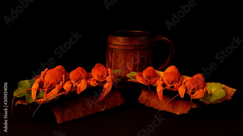 Two servings of delicious appetizing crayfish on improvised plates of rough bark and ceramic beer mug on black background. Concept, delicacies, food, gourmet, restaurant, table setting.