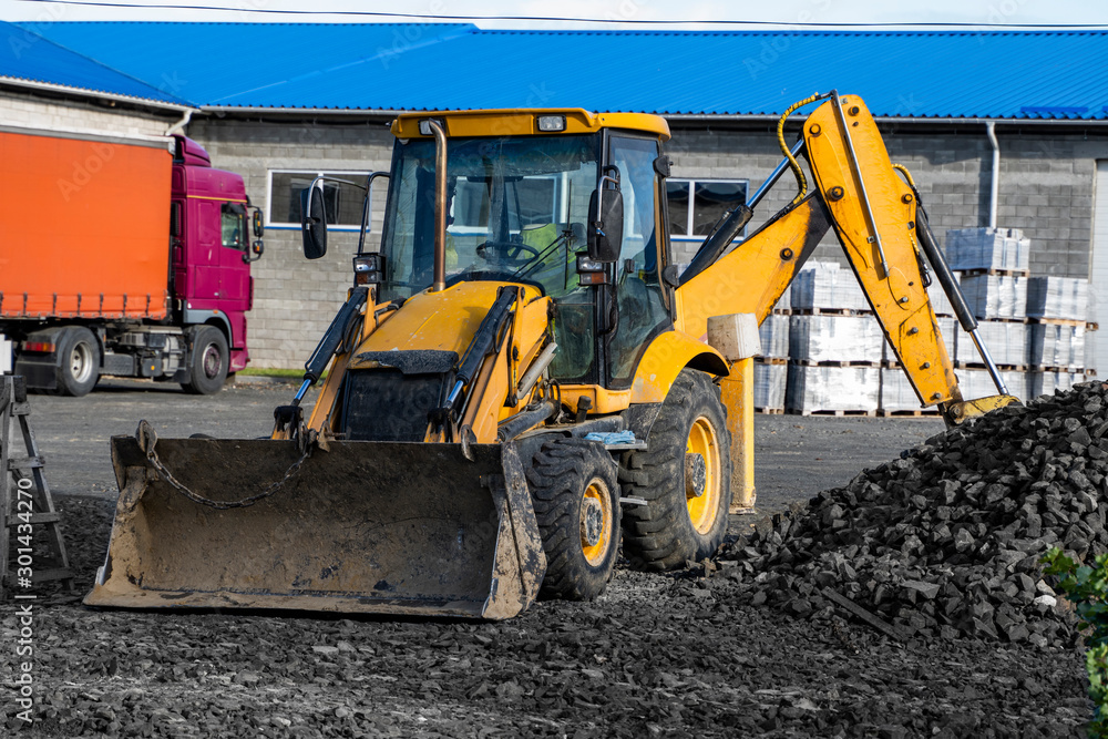 The yellow all-wheel drive backhoe loader stands on the yard ready for workind on construction site.