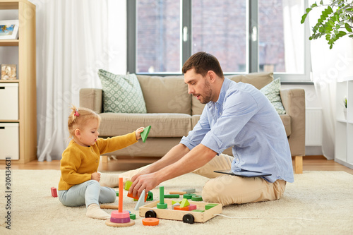 family, fatherhood and people concept - happy father and little baby daughter playing with wooden toy toy blocks kit at home