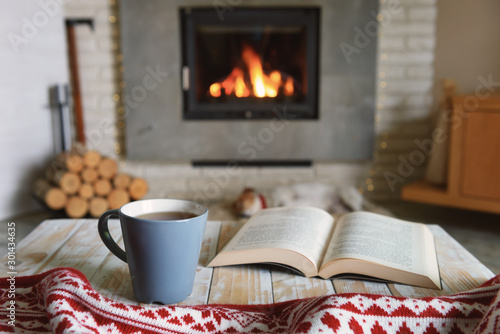 Canvas Print Hygge concept with open book and cup of tea near burning fireplace