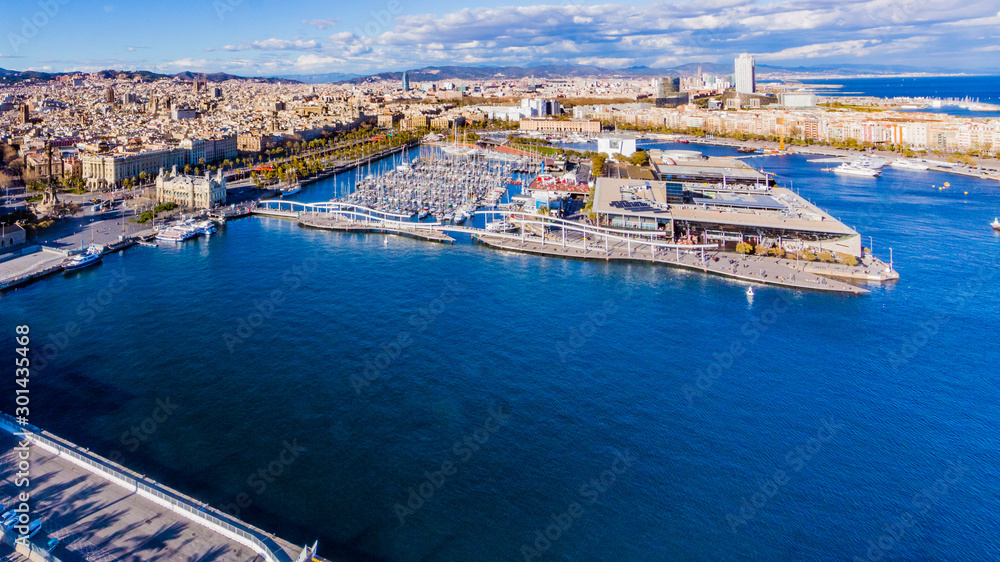 Aerial view of the old port with sports boats and part of the city of Barcelona, ​​sunny and calm day with a blue sky and white clouds in Spain