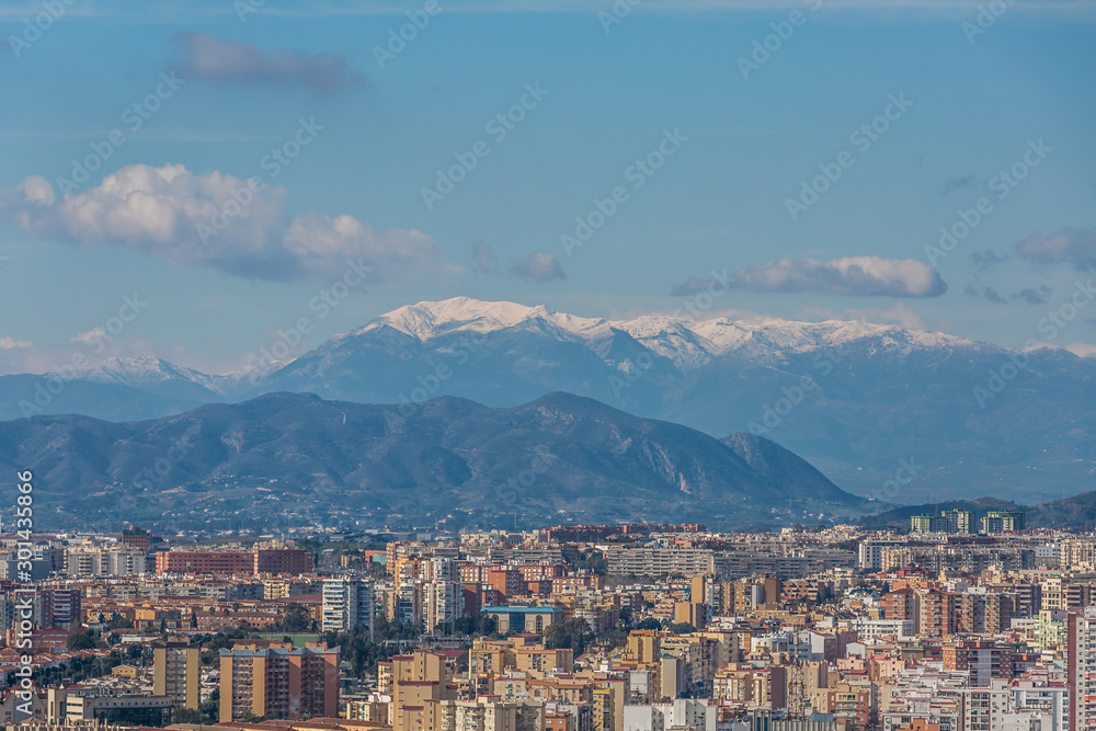 Aerial view of the city of Malaga with its houses and buildings with snowy mountains in the background, sunny day in the province of Malaga, Spain