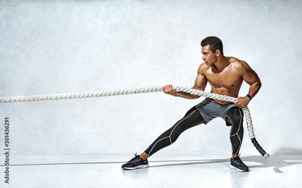 Strong man pulling rope. Photo of sporty man on grey background. Strength  and motivation. Side view. Full length Stock Photo