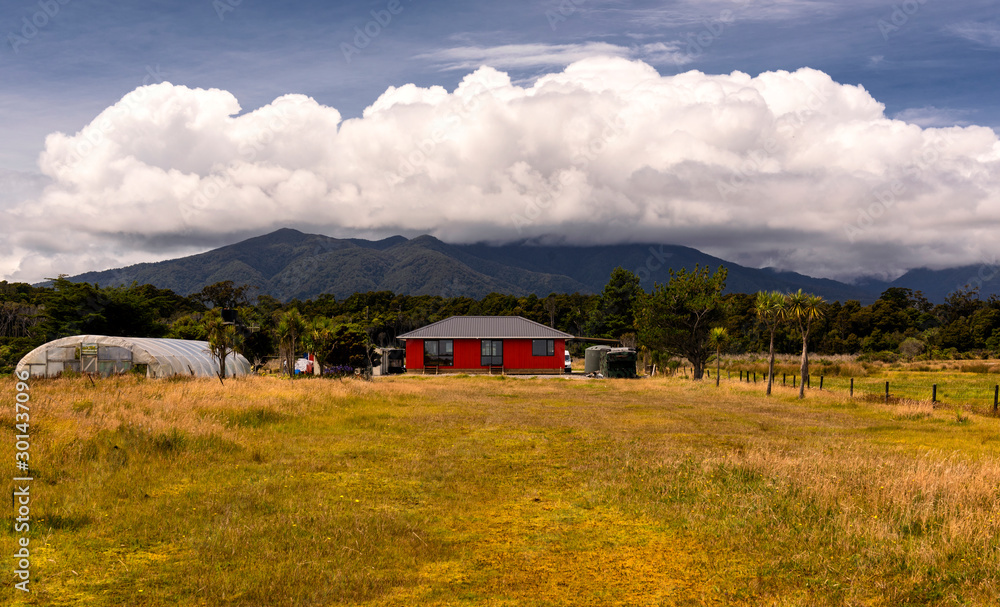 small farm with modern, red house in front of magnificent mountain scenery with wide cloud band