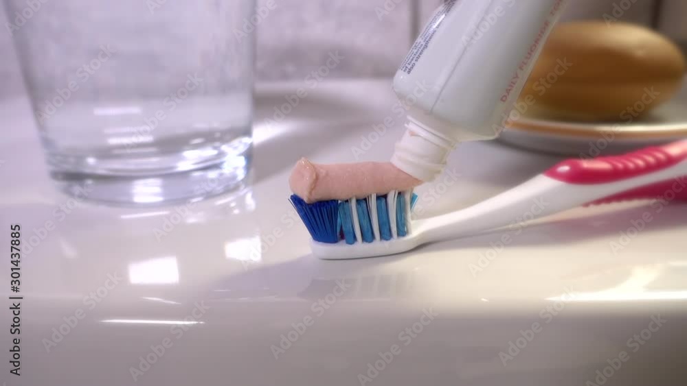 Slow motion close POV shot of fluoride toothpaste being carefullly squeezed from its tube onto a toothbrush, which is resting on a bathroom sink. Slow motion close POV shot of fluoride toothpaste being carefullly squeezed from its tube onto a toothbrush, which is resting on a bathroom sink.