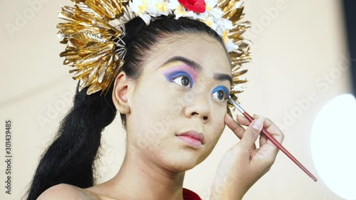 Pretty female balinese dancer coloring her eyelids in makeup room. Shot in 4k resolution photo