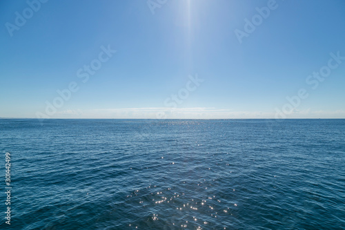 Glaring midday sun creating a beam in the middle of shot giving the calm ocean sparkle
