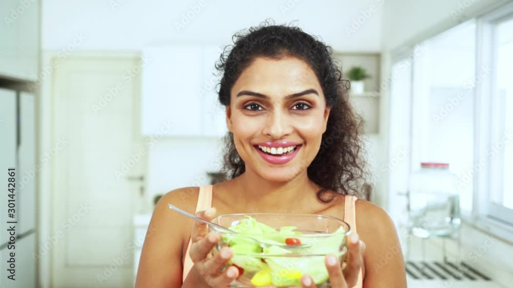 Slow motion of pretty Indian woman smiling at the camera while holding a bowl of fresh vegetables salad in the kitchen at home Slow motion of pretty Indian woman smiling at the camera while holding a bowl of fresh vegetables salad in the kitchen at home