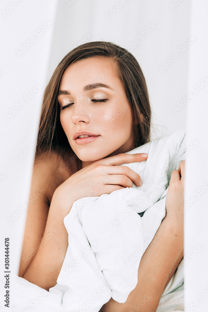 A young beautiful woman with long hair wakes up on the white bed at home, A young beautiful woman with long hair wakes up on the white bed at home,