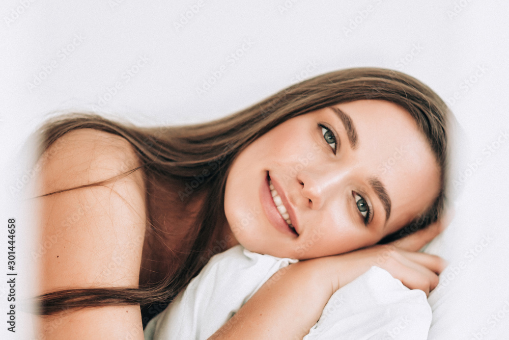 A young beautiful woman with long hair smiles and wakes up on the white bed at home A young beautiful woman with long hair smiles and wakes up on the white bed at home