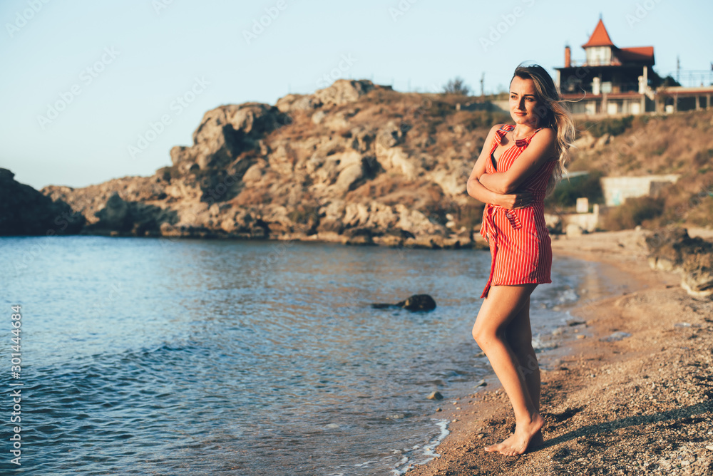 Beautiful Girl in red dress on the background of sea and rocks
