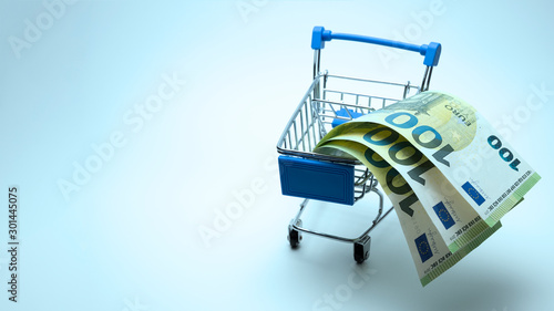 Banknotes of 100 euros in a stroller for shopping. Spend three hundred euros and get a bonus. Blue tinted background. Copy space. The concept of discounts, Template for black friday, cyber monday. photo