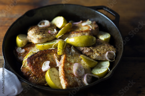 Fried pork chops with apples in a cast iron skillet. 