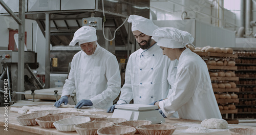 Very charismatic baker man with a large smile and his colleagues forming the dough to baking the bread, process of making the bread , food industry