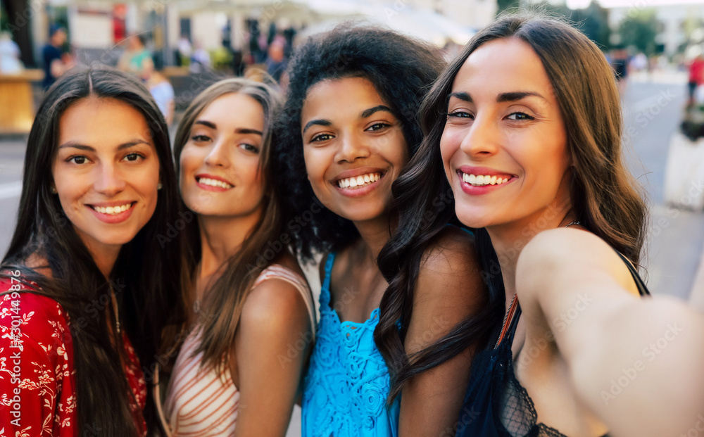 Fototapeta premium Luxury selfie lovers. A selfie of three brunettes and one girl with fair hair, who are smiling with eternal joy while looking at the camera.