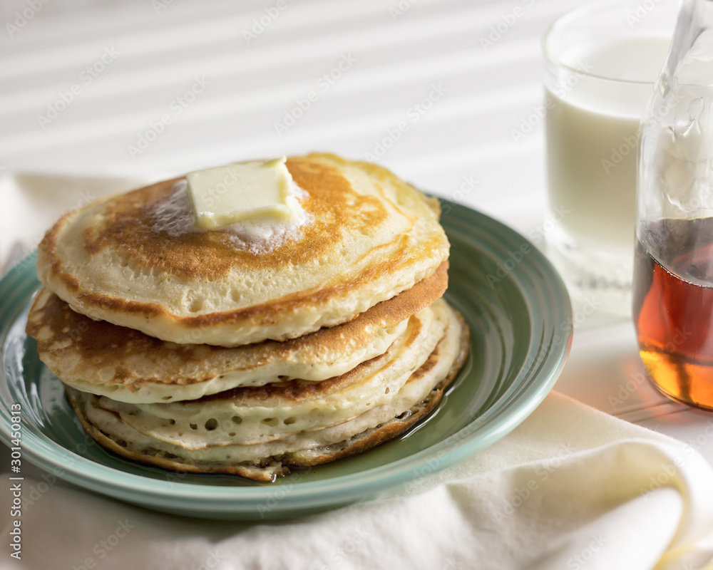 Pat of butter melting on a stack of hotcakes with glass of milk and cloth napkin. Pat of butter melting on a stack of hotcakes with glass of milk and cloth napkin.