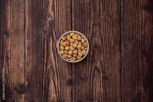 Overhead view of roasted hazelnuts in a bowl on rustic wood background.
