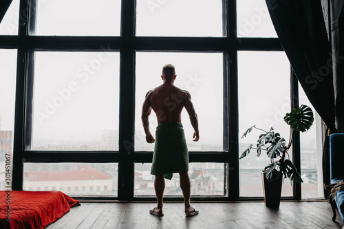 silhouette of a sporty sexy bodybuilder man by a large window with a city view.
