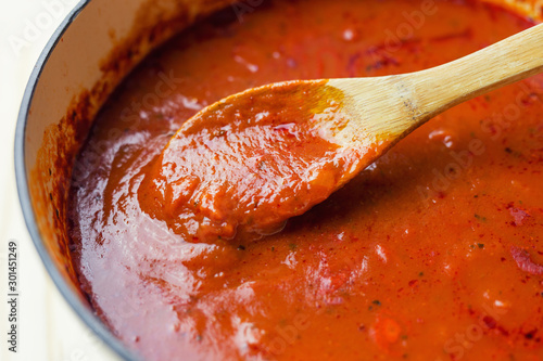 Wooden spoon stirring a pot of marinara sauce. Close up view. 