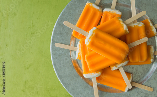 Overhead view of a bunch of orange dreamsicle pops on a serving tray. Top view with copy space, green background. 