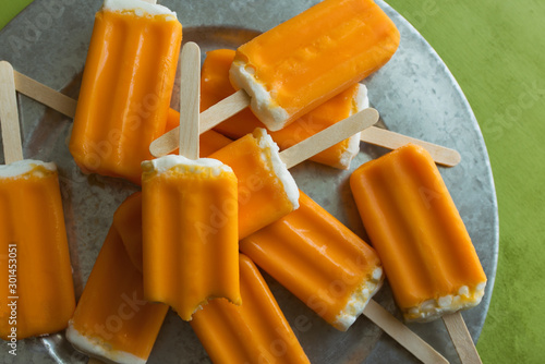 Many orange creamsicle pops on a galvanized steel tray against a lime green background. Top view. 