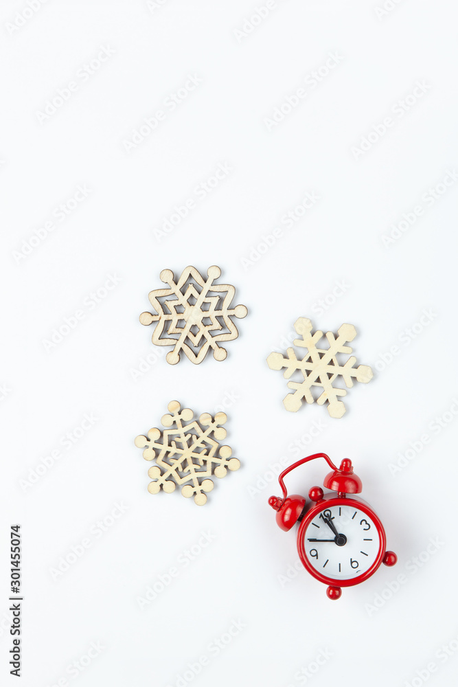Simple Christmas composition. Small analog red clock, wooden snowflakes on white background. Minimal style flat lay, for social media. Top view. Celebration concept Simple Christmas composition. Small analog red clock, wooden snowflakes on white background. Minimal style flat lay, for social media. Top view. Celebration concept