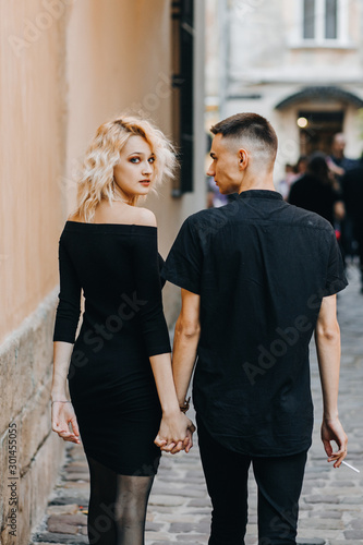 Fashionable couple walking down the street holding hands. Gorgeous blonde woman looking back