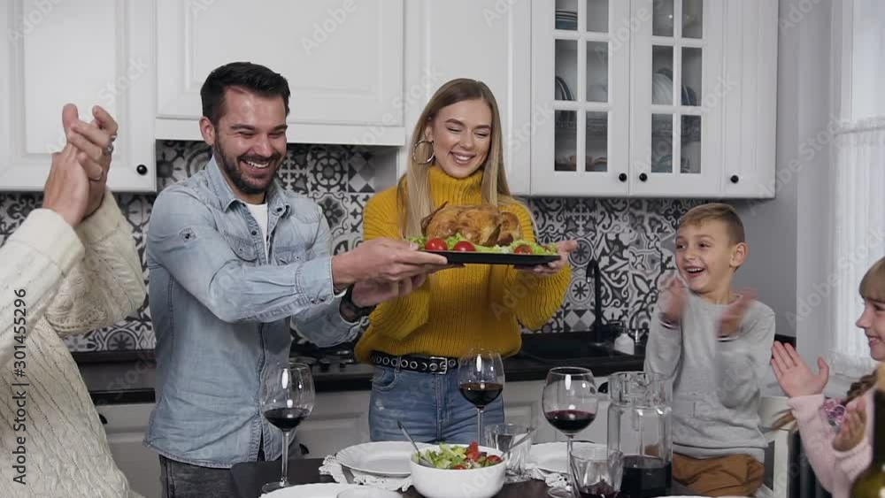 Smiling happy young man and woman putting on festive table roast turkey during celebration the Thanksgiving day Smiling happy young man and woman putting on festive table roast turkey during celebration the Thanksgiving day