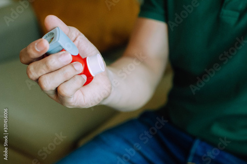 A young man is holding an asthma inhaler device while sitting on a couch